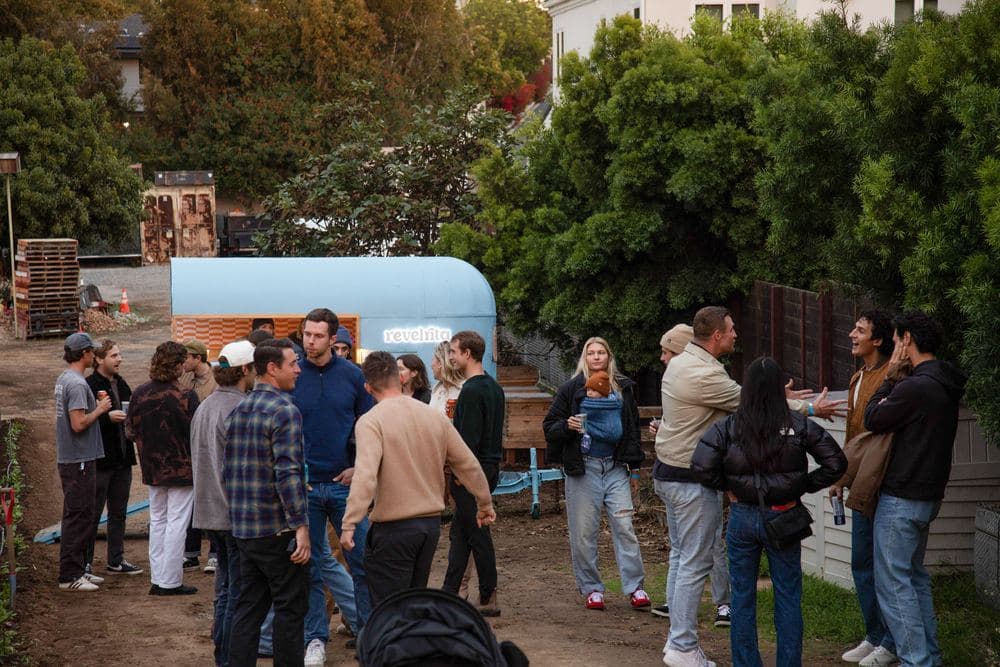 A crowd with drinks around the cart in a backyard