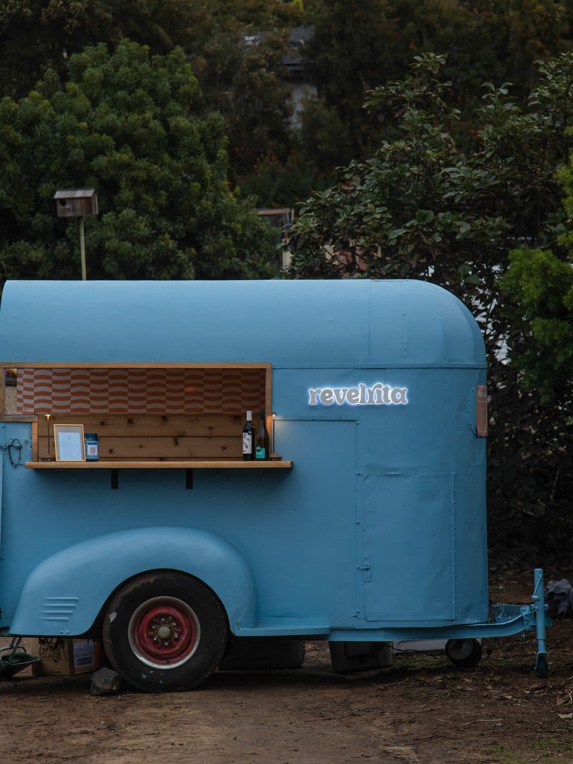 The sky blue cart with its sign lit up in a garden at dusk
