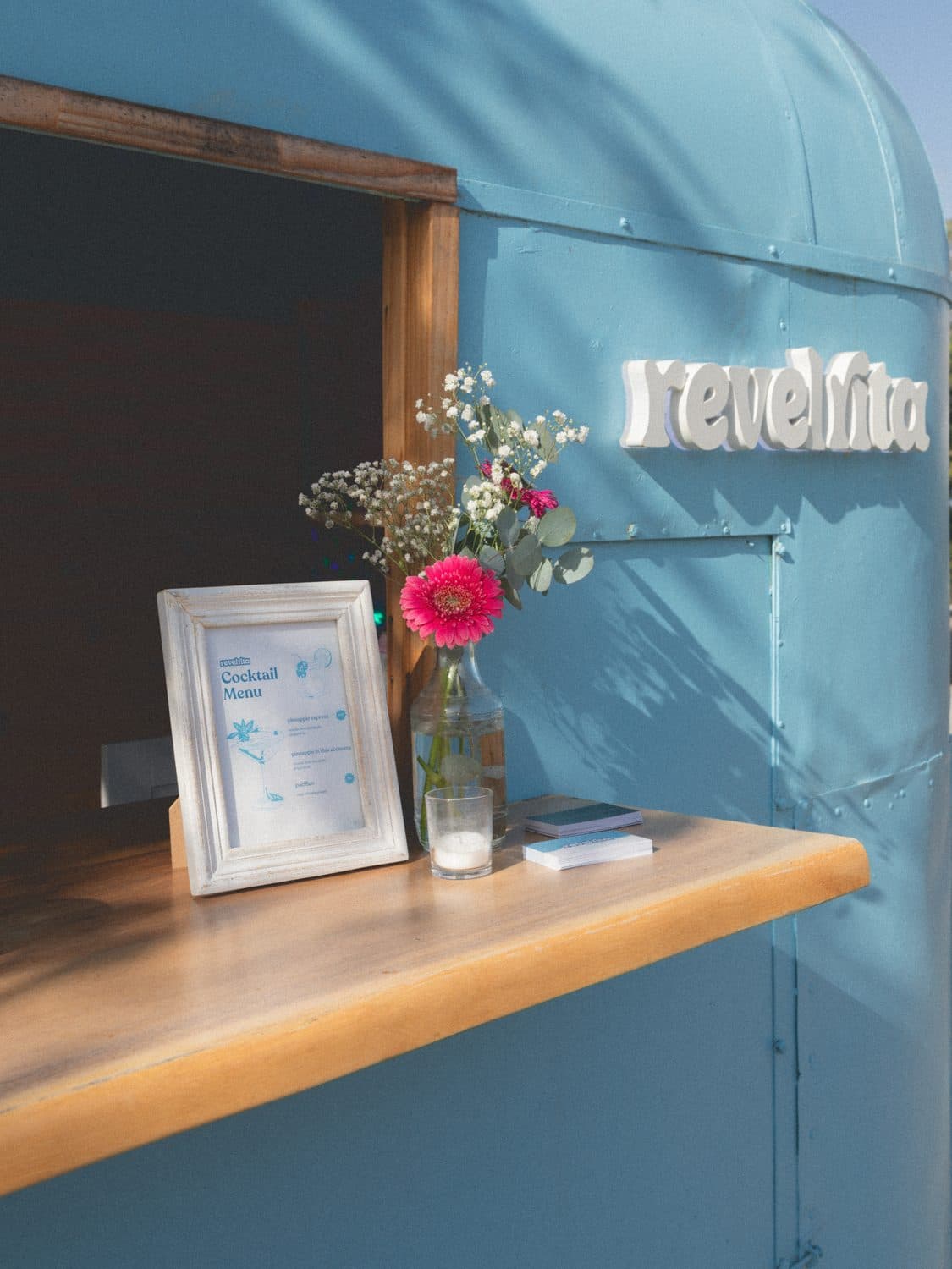 The cart window with fresh flowers, a framed cocktail menu and the revelrita sign